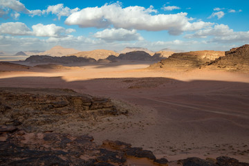 Fototapeta na wymiar Kingdom of Jordan, Wadi Rum desert, sunny winter day scenery landscape with white puffy clouds and warm colors. Lovely travel photography. Beautiful desert could be explored on safari. Colorful image