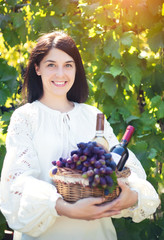 Young woman with a basket of grapes and bottles of wine at the vineyard.
