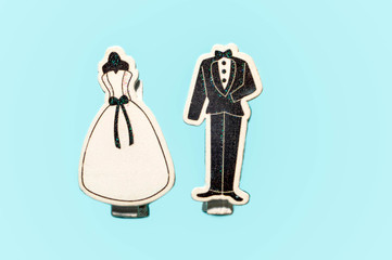 top view of decorative classic white wedding dress and black groom tuxedo clips together isolated on blue surface with copy space, greeting concept