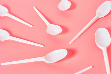 White disposable spoons scattered on pink background. Concept of save environment, ecology,...