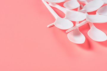 Heap of white disposable spoons scattered on pink background. Concept of save environment, ecology, recreation on picnic, party and other events. Copy space