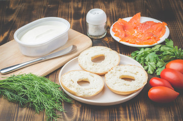 cooking of a food with round toast with cheese, red fish, tomatoes and vegetables/Healthy food with round toast, red fish, vegetables and cheese on wooden table.