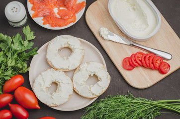 cooking of a food with round toast with cheese, red fish, tomatoes and vegetables on black table/Healthy food with round toast, red fish, vegetables and cheese on black table. Top view.