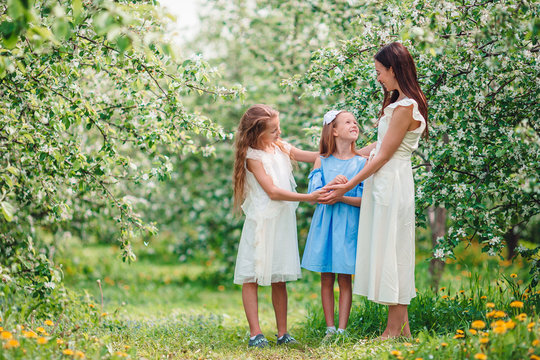 Adorable little girls with young mother in blooming cherry garden on beautiful spring day