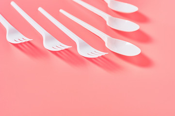 Row of white disposable spoon and fork scattered on pink background. Concept of save environment, ecology, recreation on picnic, party and other events. Copy space