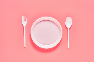 Disposable plastic utensils scattered on pink background. Concept of save environment, ecology, recreation on picnic, party and other events