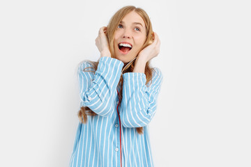 Happy attractive young girl in pajamas listening to music on headphones on white background
