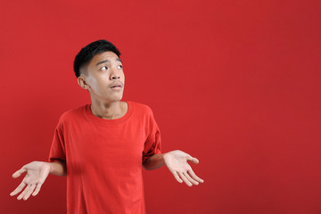 I don't know. Young man isolated on red background, showing helpless gesture with arm and hand