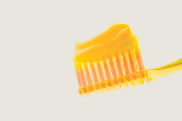 Yellow plastic toothbrush with melon toothpaste on an isolated background.