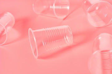 Disposable plastic glasses scattered on pink background. Concept of save environment, ecology, recreation on picnic, party and other events