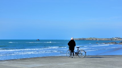 A woman and is bicycle in front of the sea at Saint-Malo in Brittany. France - obrazy, fototapety, plakaty