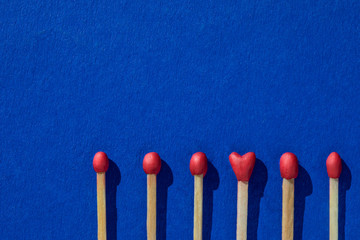 Matchsticks with a red heads with heart shaped match among others on a classic blue background. Concept of perfect match, fire of love and passion. The one and only. Flat lay, top view and copy space.