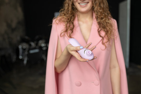 Female hand is holding womanizer sex toys on a pink background. Purpple Sex toys in the hand of a woman. Place for text. Sex shop concept. Shop for adults. Minimal dildo vibrator for clitoris.