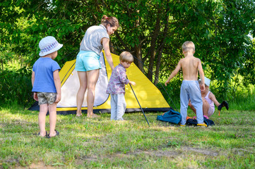 a large mother with four little children toddlers sets up a camping tent. family with little children have fun spending summer holidays in nature outdoor