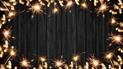 Silvester festive background - Frame made of sparklers and bokeh lights on rustic wooden black...