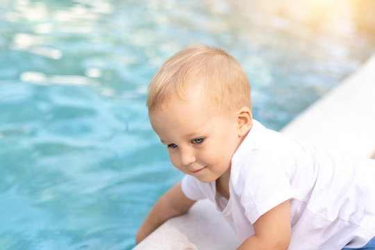Cute adorable little caucasian blond smiling todller boy kid treing water temperature pool edge before swimming. Happy child wear white t-shirt near poolside enjoy summer vacation travel with family