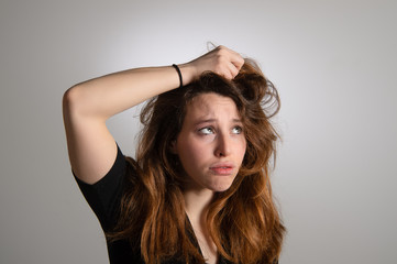 Fototapeta premium Portrait of frustrated young girl holding her long brown hair. Disappointed expression in female face. Isolated on grey background. Emotions...
