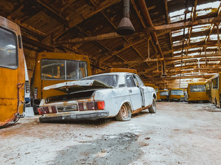 old retro car abandoned between yellow rusty minibuses at an abandoned central bus station