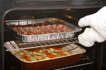 An oven full of sausages with bacon and roasting vegetables