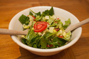 A fresh green salad in a bowl with serving spoons