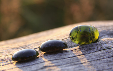 3 black jade translucent gemstones on wood, one different