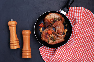 Roasted pork steak in frying pan on black background