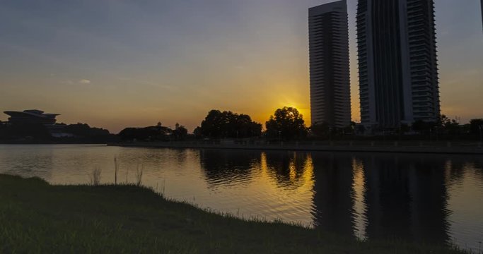 Sunset time lapse on the Putrajaya lake with four skyscraper behind the lake. The buildings reflecting in the lake. When it gets dark the lights come on and illuminating the scenery in awesome light. 