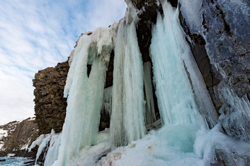 An upward view of a wall of ice as the water falls down over the rock cliff. The background is blue...