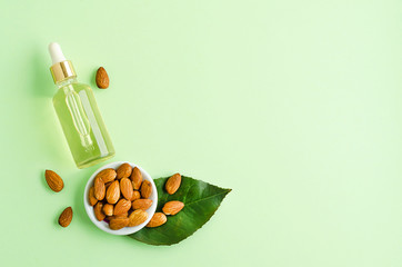 flat lay almond oil and whole nut for skincare, massage, cooking on green background.