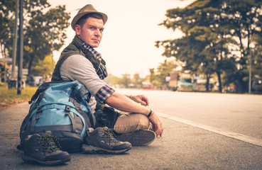 Young man Caucasian hiking with backpack sitting on road outdoors, handsome man tourist on holiday