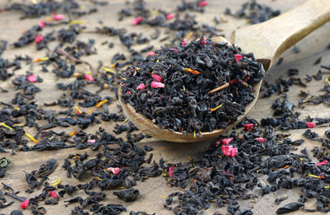 blended tea. black tea with dry flower petals. dry black tea leaves in a wooden spoon. close up