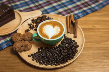 Latte art coffee cup and beans, cinnamon on a wooden plate on table.