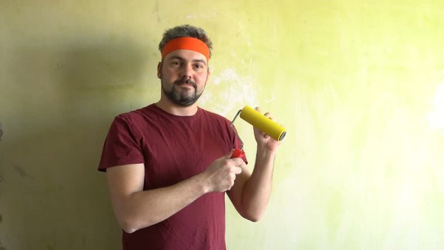 Bearded man against the wall. Good mood. In the hands of a construction roller for wallpaper. Repair work in the room. Frick. Retro style. Green wall.
