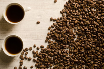 Сups of hot coffee, scattered coffee beans, heather on a wooden light background. Romantic evening, breakfast, dinner. View from above