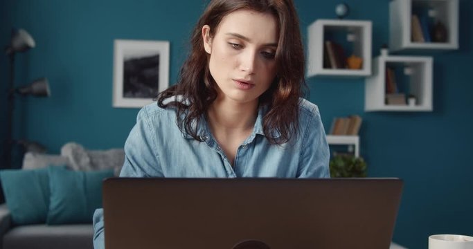 Portrait of charming young girl in casual clothing feeling sadness while looking at computer screen. Disappointed lady with curly hair working at home.