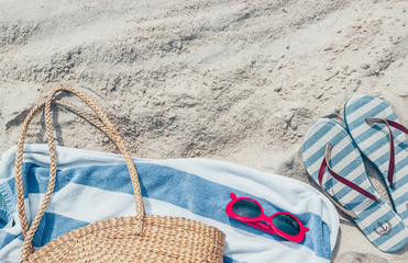 Straw bag, sunglasses and flip flops on a tropical sand beach. Travel, vacation concept.