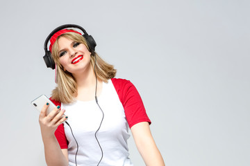 Portrait of Caucasian Girl In Casual Street Clothing Posing With Headphones And Smartphone Indoors. Against White.