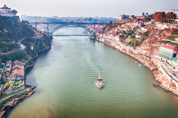 Travel Ideas. Traditional Red Tourist Travel Boat Floating in Porto City Across The Douro River in Portugal. Cityscape with Red Rooftops in Background