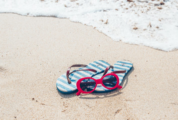 Fototapeta na wymiar Sunglasses and flip flops on a tropical sand beach. Travel, vacation concept.