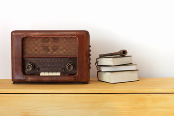 Vintage radio made of wood, old books and a pipe on a table 