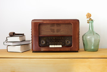 Vintage radio made of wood, old books, green vase and a pipe on a table 
