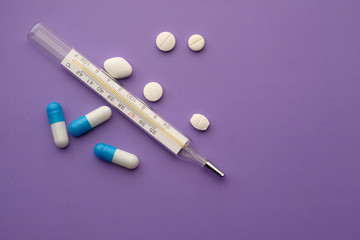 close up of pills and thermometer on purple background 