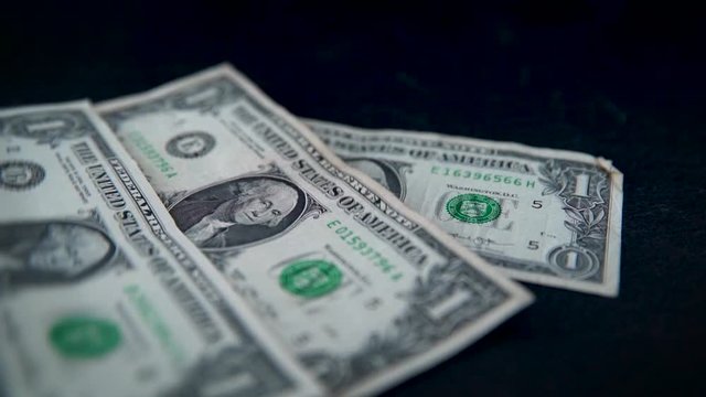 American one-dollar banknotes falling on dark table top in slow motion.