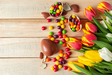 Beautiful red and yellow tulips for easter holiday. Chocolate eggs and candies on a wooden background.