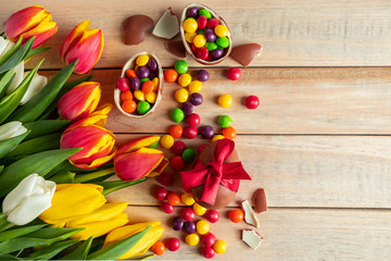 Fototapeta na wymiar Multi-colored tulips and chocolate Easter eggs on a wooden background. Festive design, place for text.