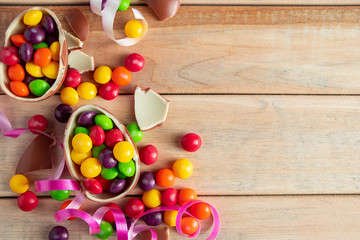 Multi-colored sweets and Easter chocolate eggs on a light wooden background.