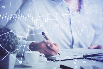 Double exposure of man's hands writing notes of stock market with forex chart.
