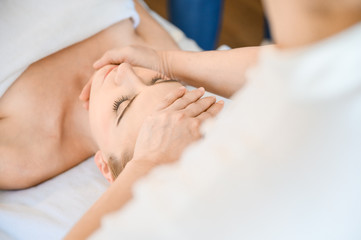 Fototapeta na wymiar Beautiful woman receiving head and facial massage in spa salon. Concept of body health care and traditional thai massage relax