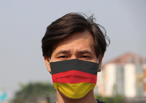 Germany Flag On Hygienic Mask. Masked Asian Man Prevent Germs. Concept Of Tiny Particle Protection Or Covid19.