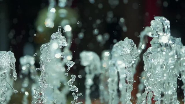 close-up slow motion of water coming out of the fountain. close-up slow motion of water grains. Close-up of the water gushing from the sprinklers in the pond. red flowers in the background.